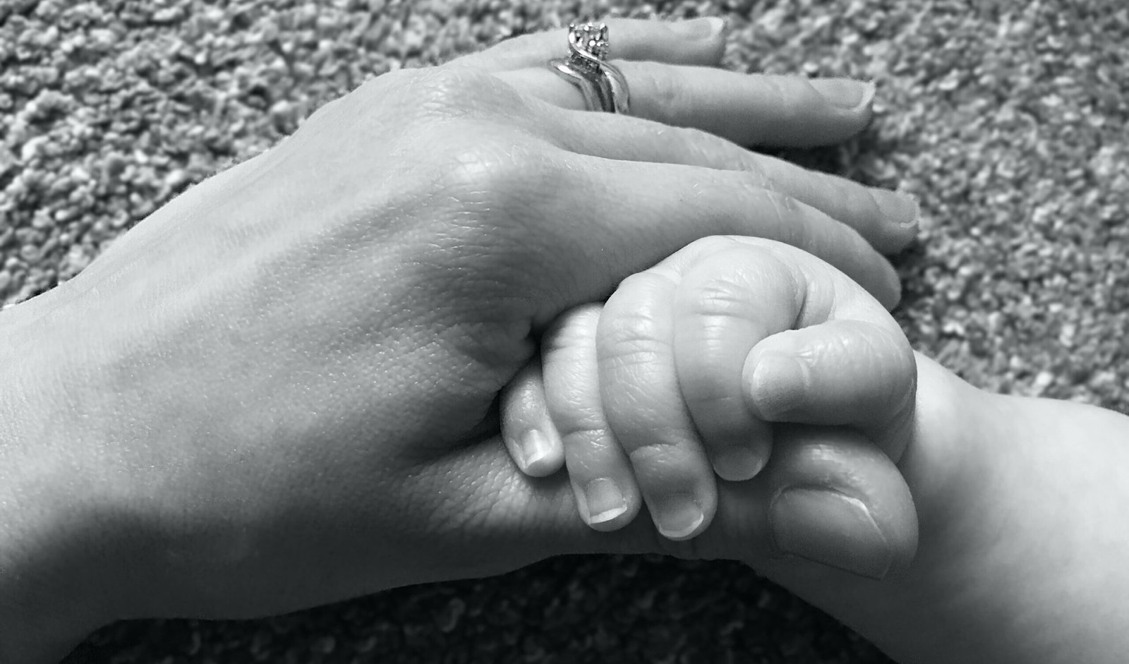 Black and white image of a woman's hand holding a baby's hand