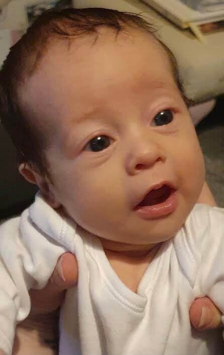 Baby with dark hair wearing a white babygrow