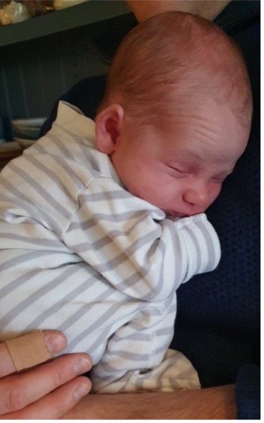 Newborn baby cuddling into parent wearing stripy baby grow
