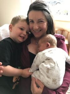 Women smiling cuddling toddler and newborn baby