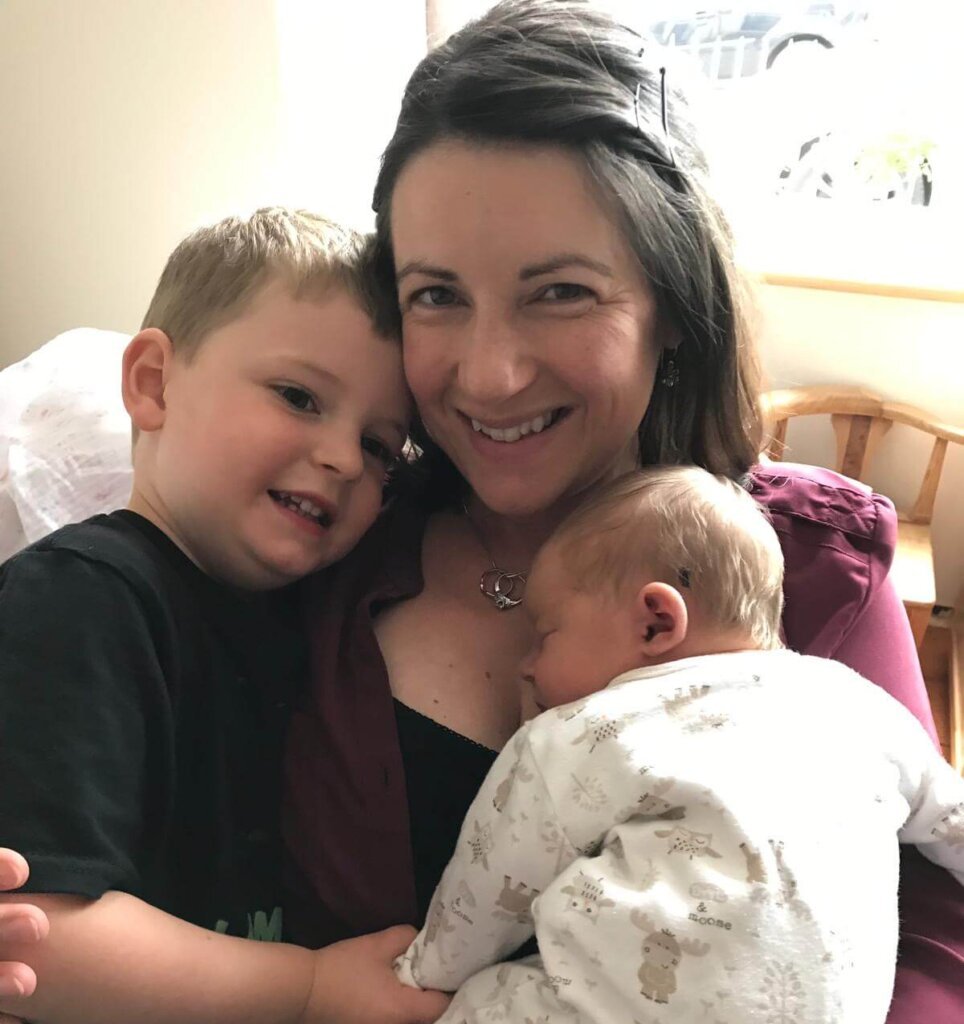 Women smiling cuddling toddler and newborn baby