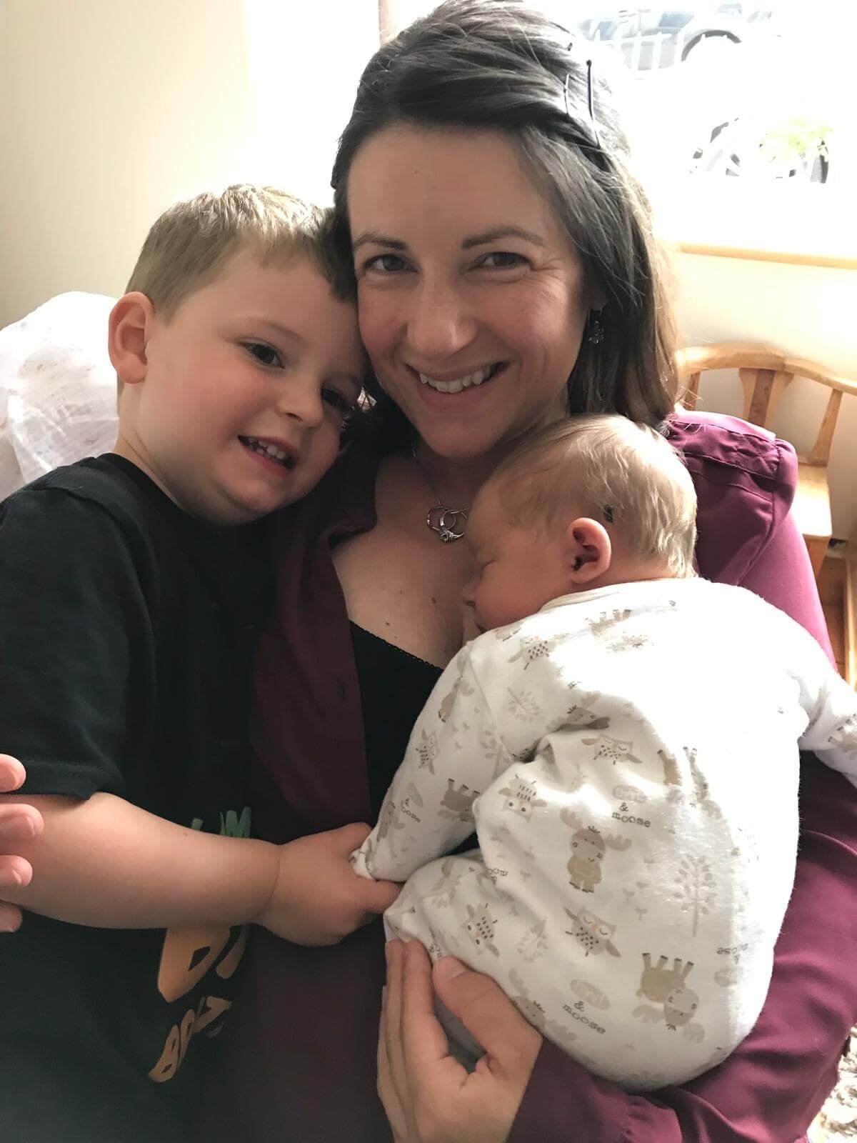 Women smiling cuddling toddler and newborn baby