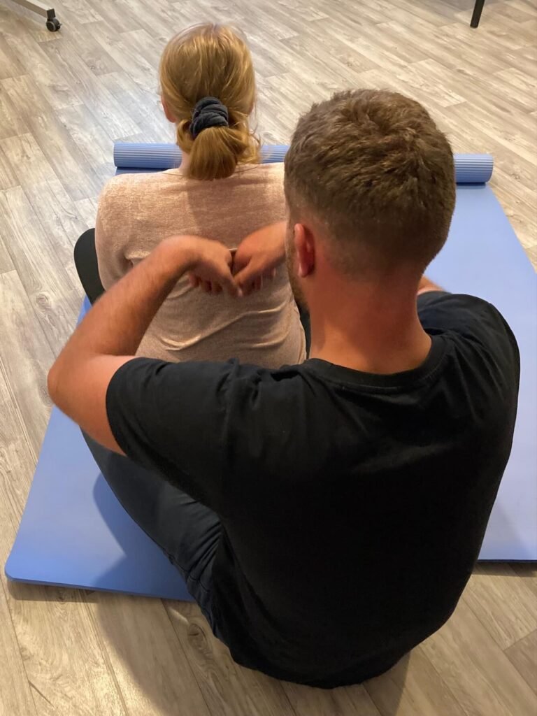 Pregnant woman sitting on a blue yoga mat being massaged by her birth partner.