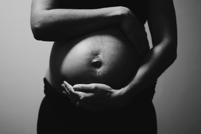 Black and white image of pregnant woman cradling baby bump.