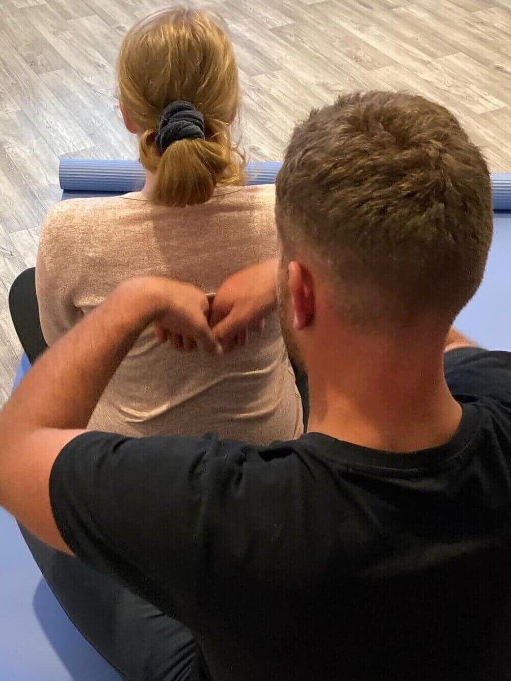 Pregnant woman sitting on a blue yoga mat being massaged by her birth partner.