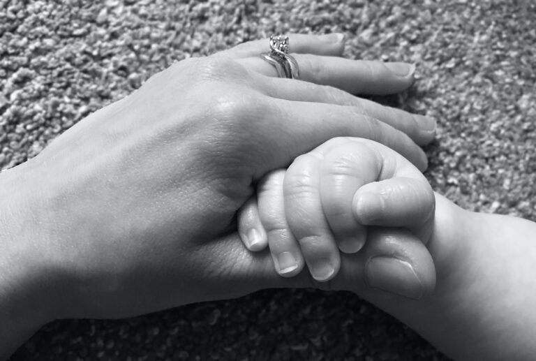 A new mother holding her newborn baby's hand at the start of matrescence.
